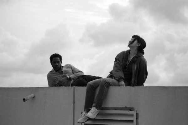 A black and white image of a man and a woman reclining on a ledge under a cloudy sky