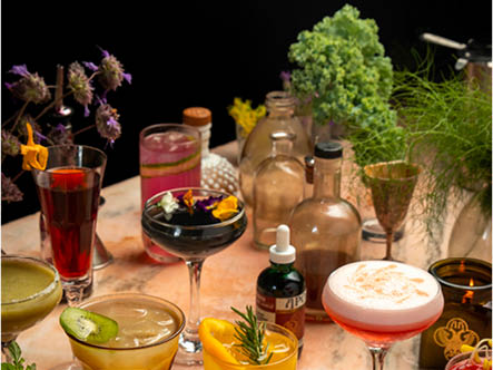 A table filled with various cocktails garnished with fruit, herbs, and tinctures