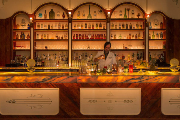 A bartender pours a drink behind the counter at a well stocked bar